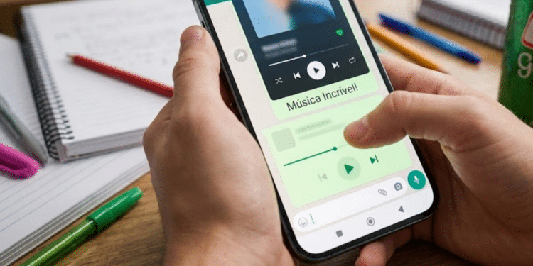 Visão em primeira pessoa de um polegar digitando uma mensagem empolgada no chat verde do aplicativo de música sobre uma mesa de estudos
