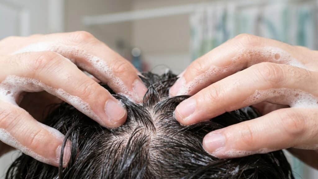Massageando espuma de shampoo na raiz do cabelo, representando a limpeza profunda do couro cabeludo