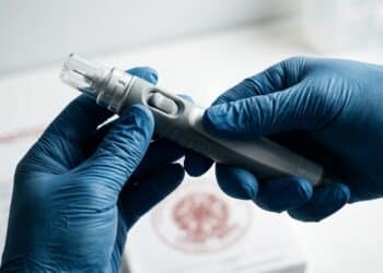 Mãos com luvas segurando autoinjetor sob iluminação dramática