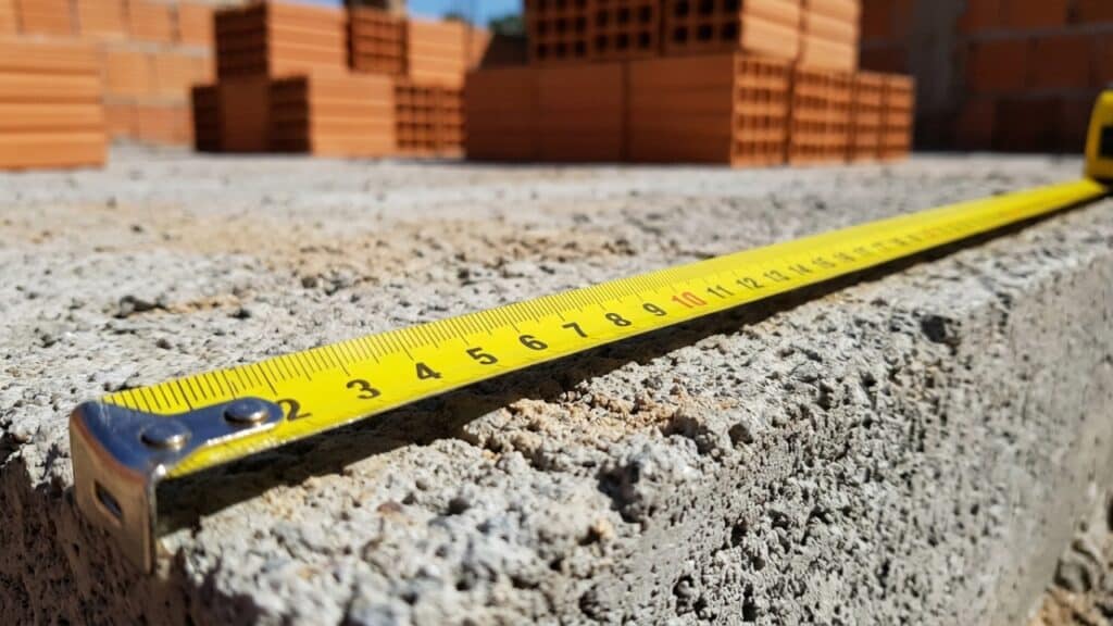 Trena medindo fundação de concreto com tijolos ao fundo, representando o início da obra de 80 metros quadrados