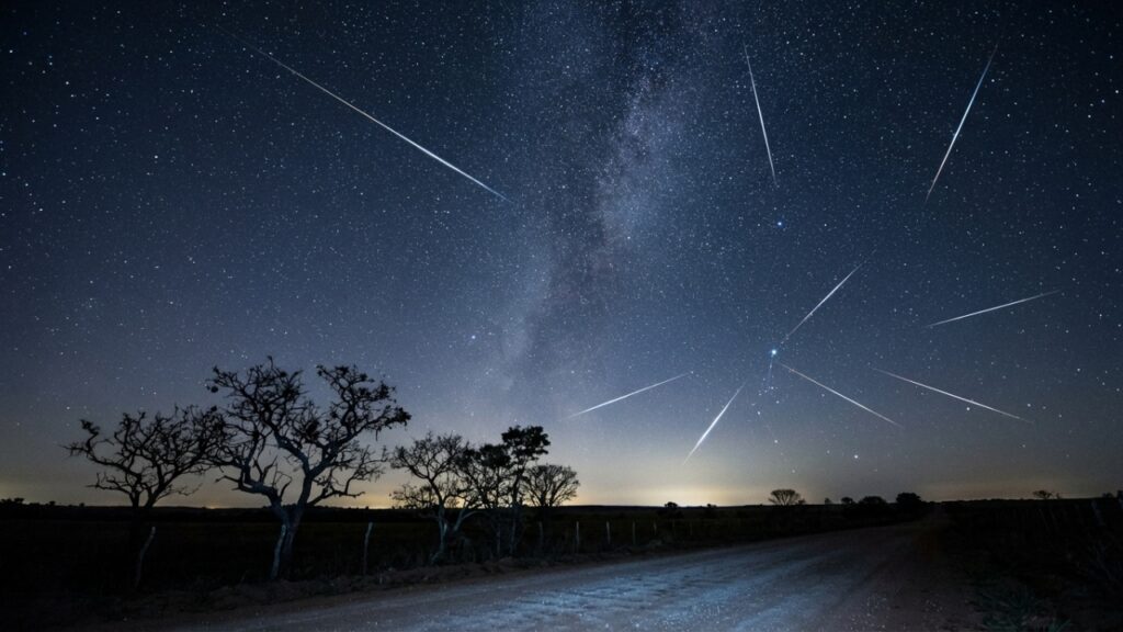 Chuva de meteoros Eta Aquáridas cruzando o céu estrelado sobre uma silhueta de vegetação brasileira