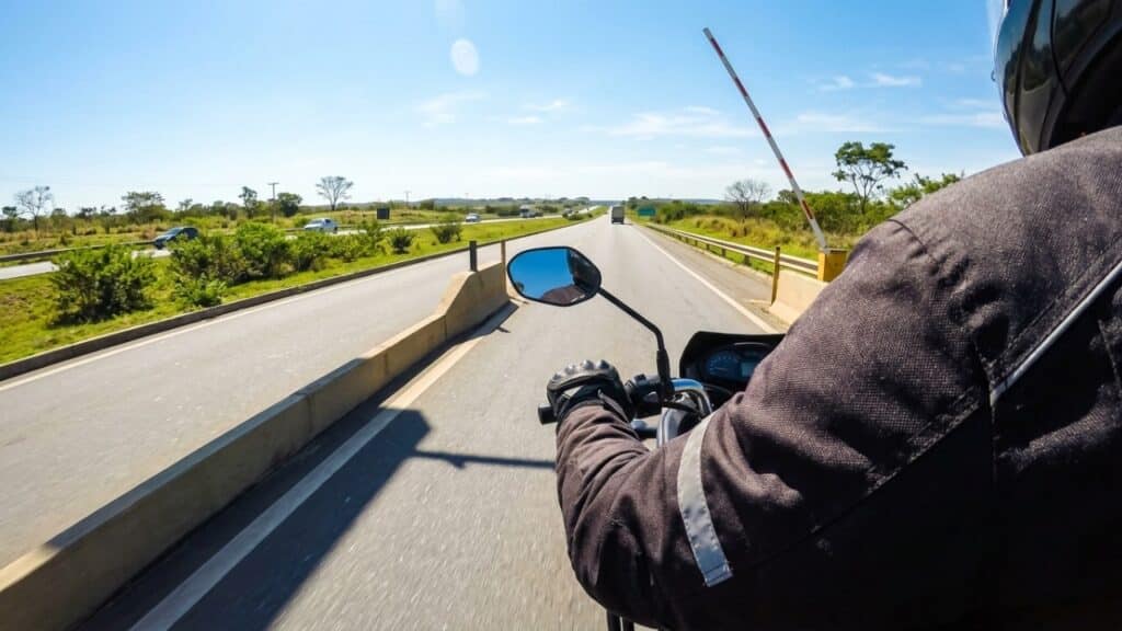 Motociclista de entregas passando livre por cabine de pedágio automática em rodovia ensolarada