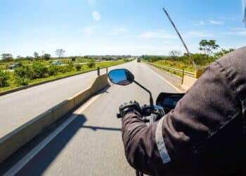 Motociclista de entregas passando livre por cabine de pedágio automática em rodovia ensolarada