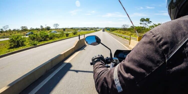 Motociclista de entregas passando livre por cabine de pedágio automática em rodovia ensolarada