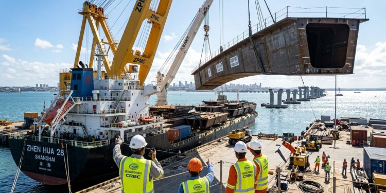 Guindastes gigantes descarregam uma grande estrutura metálica de um navio cargueiro, com trabalhadores de capacete acompanhando a operação no porto.